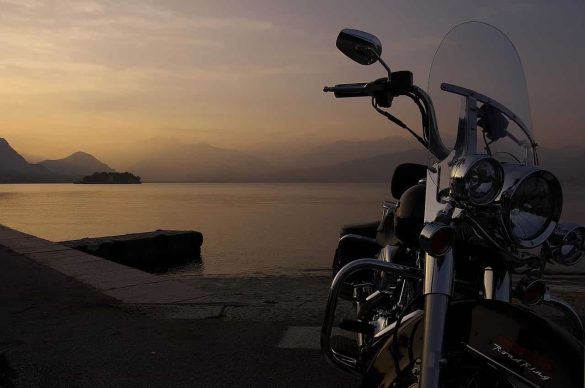 Une moto avec pare-brise chromé au bord d'un lac paisible au coucher du soleil.