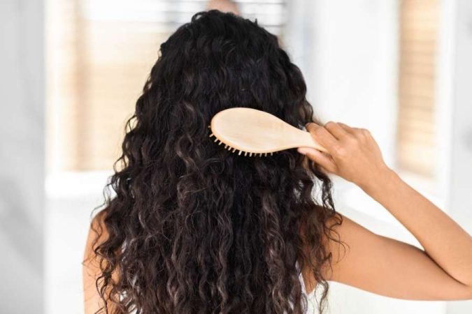 Une femme brune se brosse délicatement ses longs cheveux bouclés avec une brosse en bois.