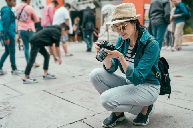 Une touriste accroupie prend des photos de rue en voyage avec un appareil photo reflex dans une zone piétonne animée.