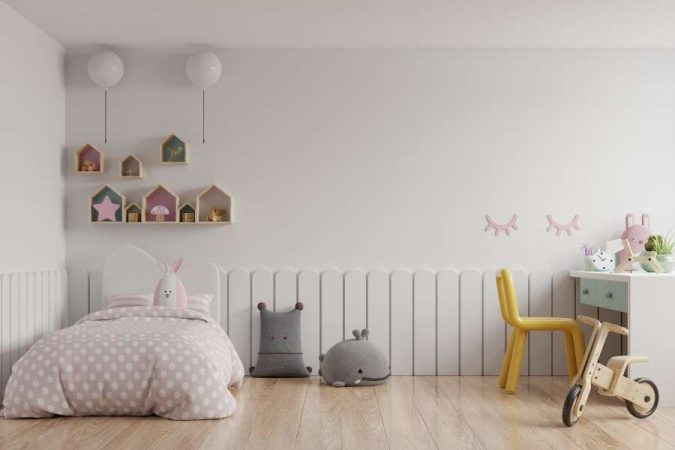 Un lit au sol enfant 90x200 avec une parure de lit rose à pois, dans une chambre décorée de façon ludique avec des étagères en forme de maison.
