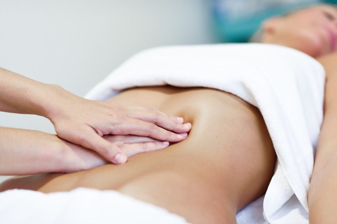 Mains d'un praticien effectuant un massage viscéral sur le ventre d'une femme allongée.
